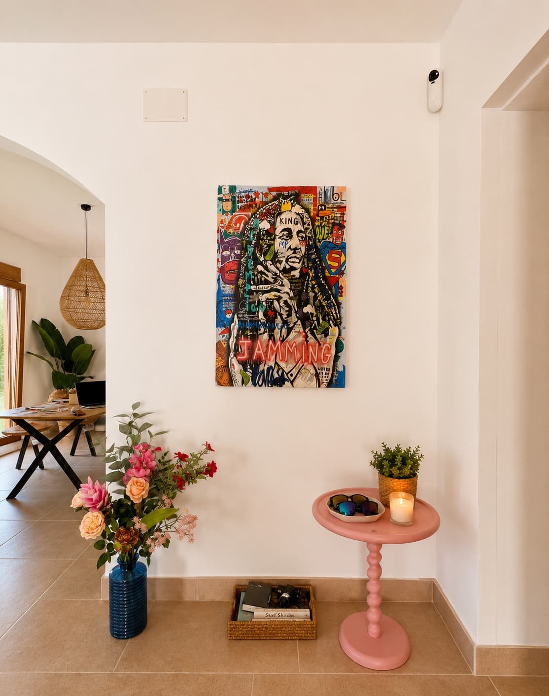 A hallway corner with a Bob Marley canvas, fresh flowers and a pink side table