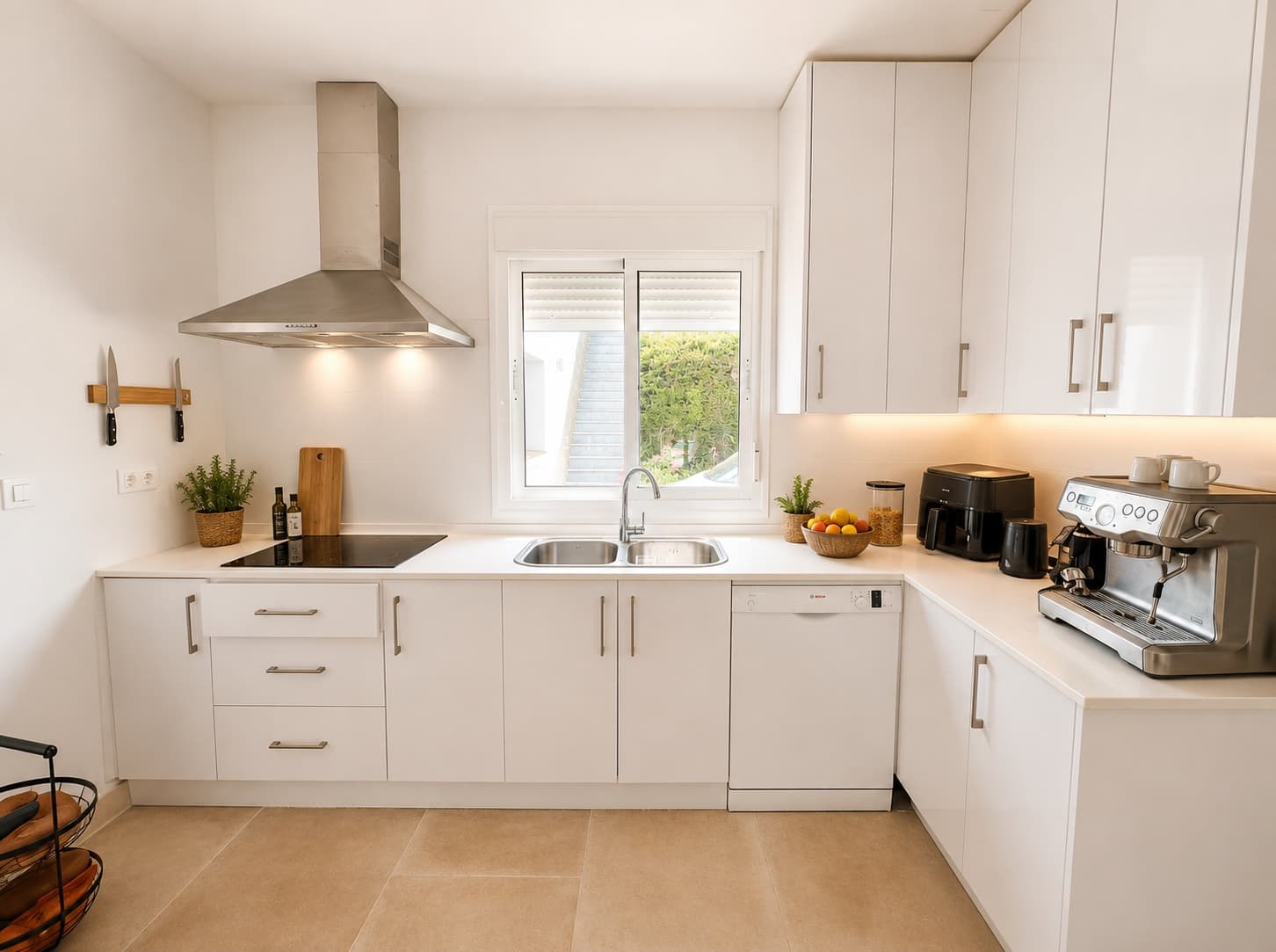 A bright white kitchen with a serious espresso machine and a bowl of fruit