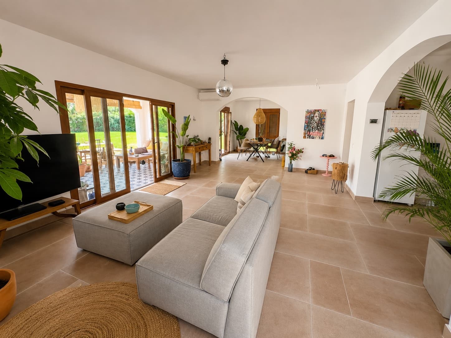 The open living room: linen sofas, plants, a disco ball and the garden through the doors