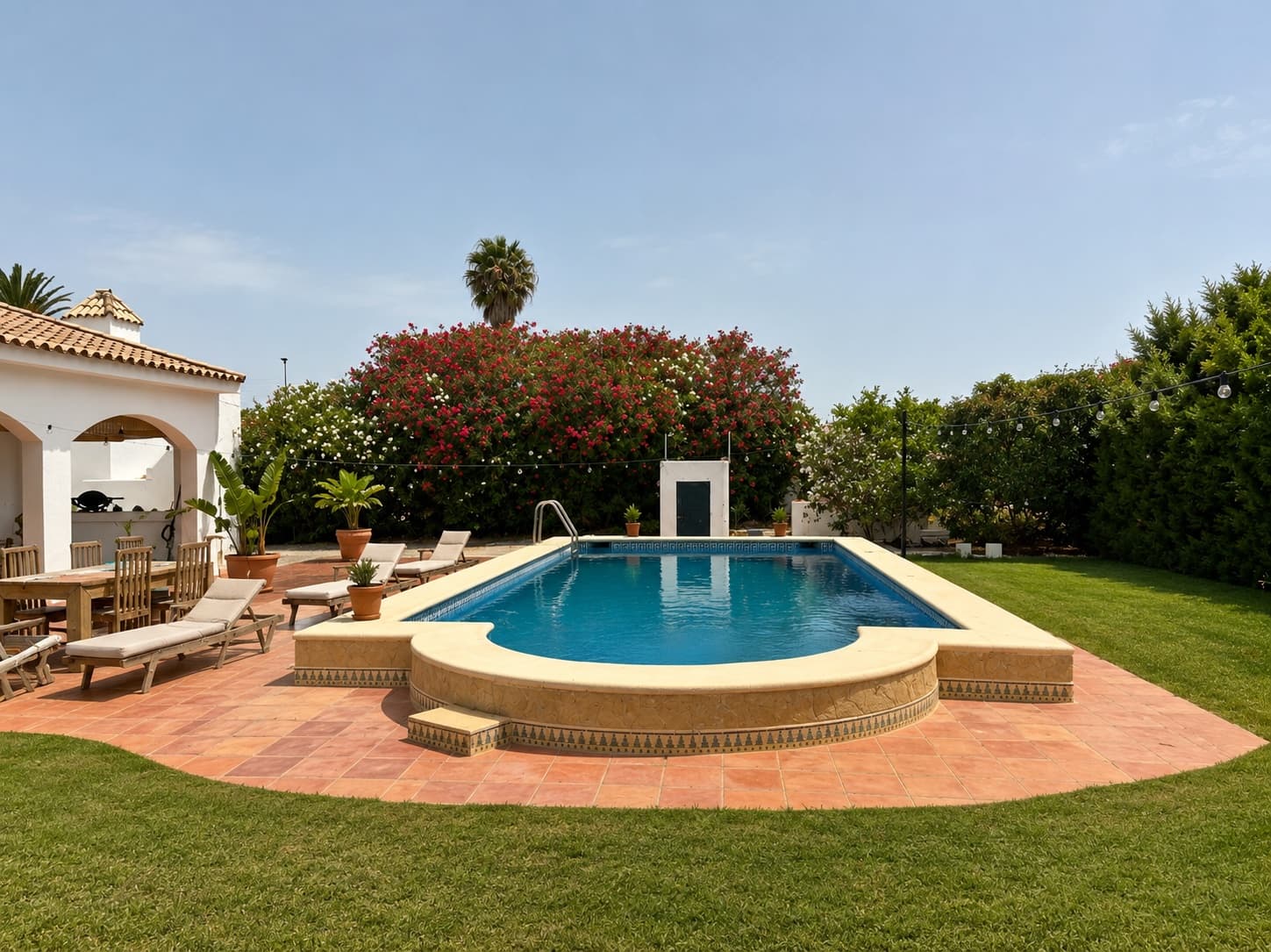 A pool and terrace in full Andalusian daylight, flowers in bloom behind